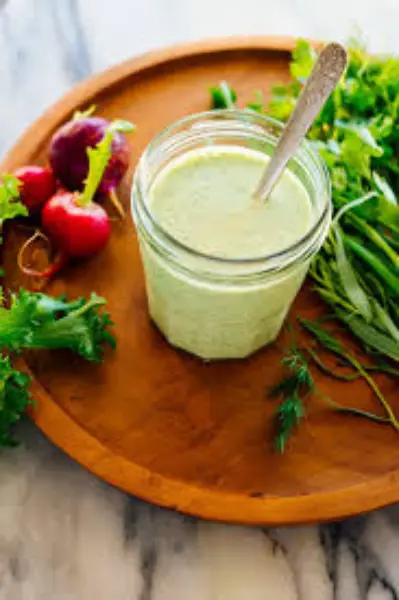 A variety of colorful sauces and salad dressings served in small bowls, surrounded by fresh tomatoes, parsley, garlic, and lemon slices