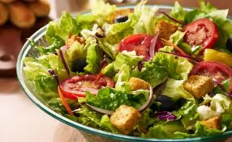 A fresh Caesar Side Salad served in a white bowl, featuring crisp romaine lettuce, shredded parmesan cheese, golden garlic croutons, and creamy Caesar dressing drizzled on top.